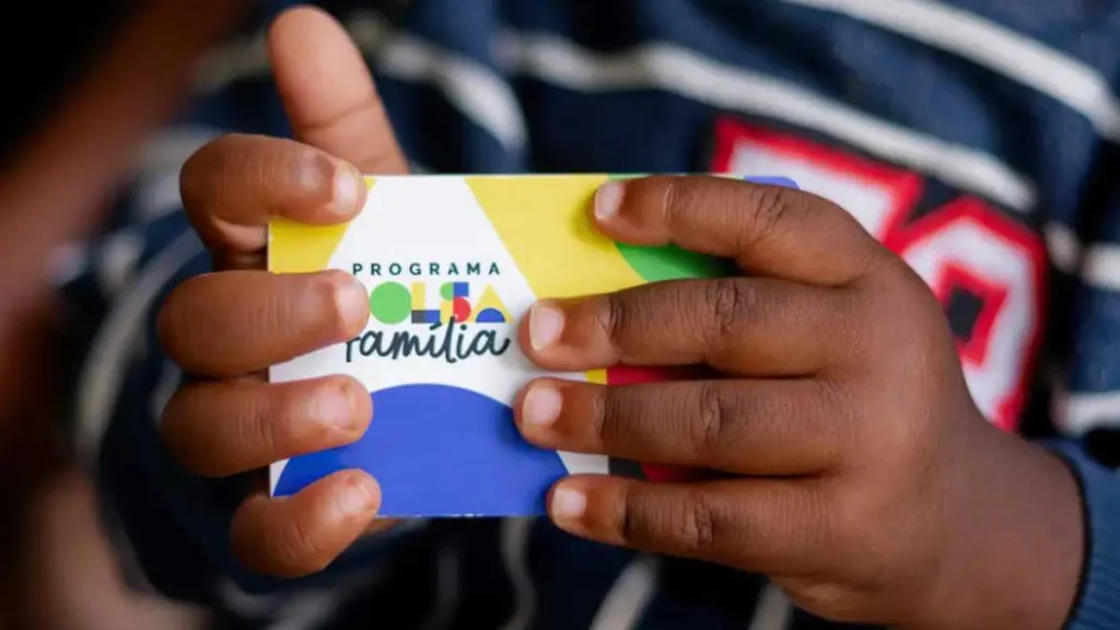 Criança negra segurando o cartão do Bolsa Família.