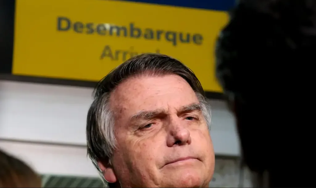 Jair Bolsonaro no aeroporto, em frente a placa de desembarque