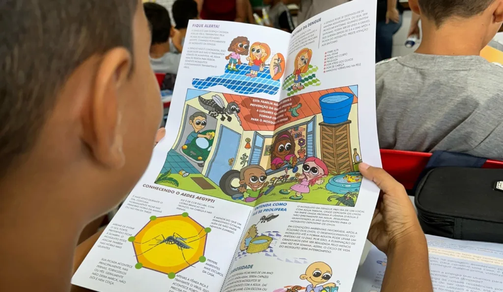 A imagem mostra uma criança lendo um infográfico sobre o combate à dengue.