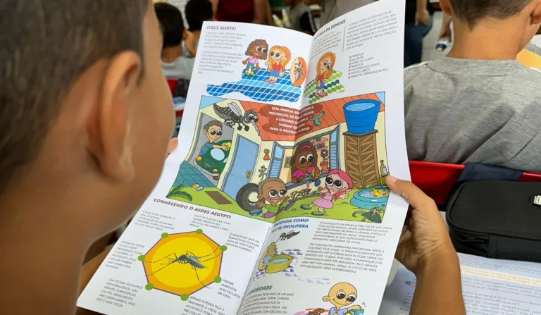 A imagem mostra uma criança lendo um infográfico sobre o combate à dengue.