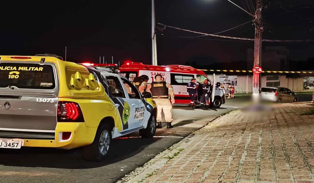 Viaturas da Polícia Militar e do Samu atendendo ocorrência de homem morto com disparos, caído na calçada.