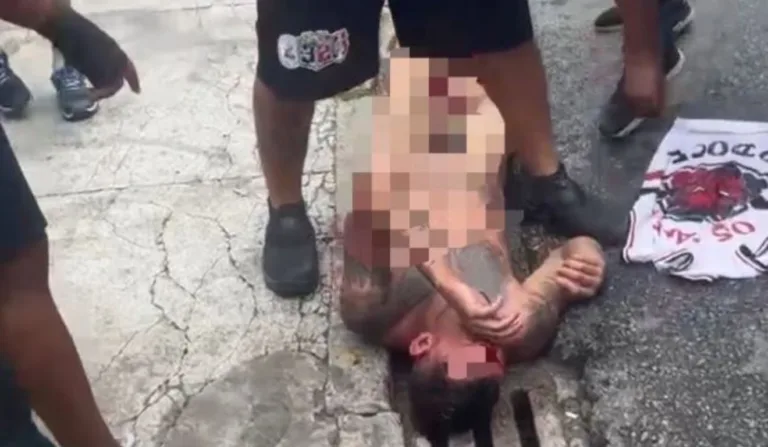 Homem caído no chão nu sendo agredido por torcedores