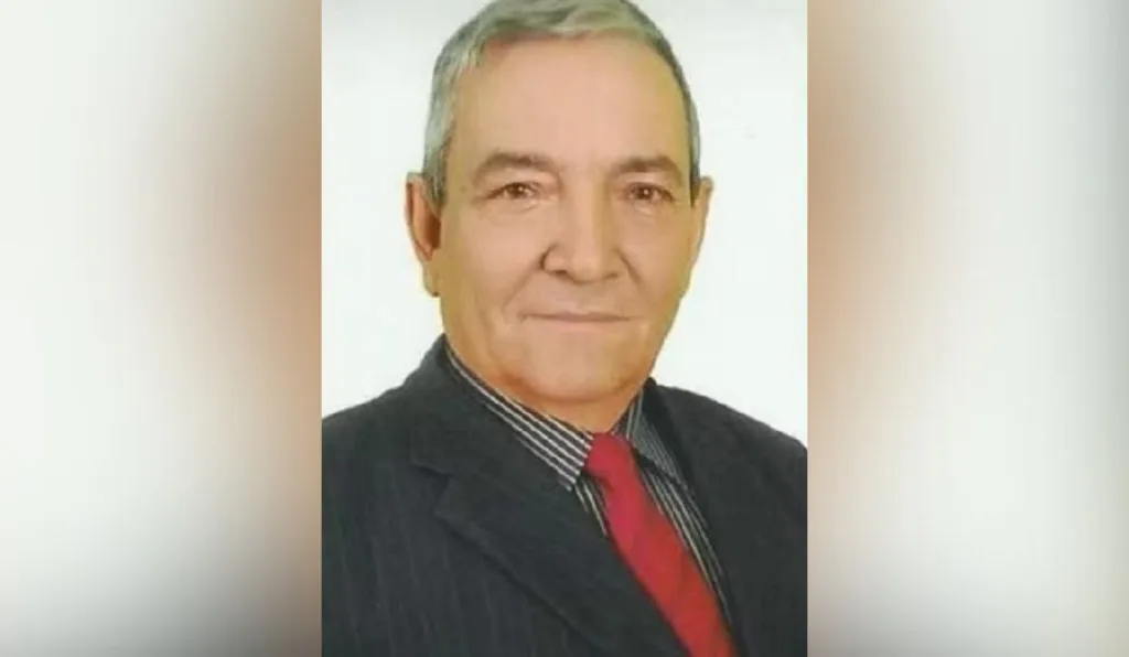 foto de um homem com cabelo branco, terno preto e gravata vermelha