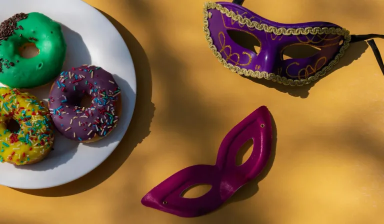 A imagem contém duas máscaras de carnaval e alguns donuts.