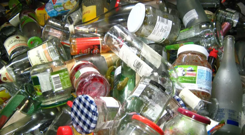 A imagem mostra uma estação de triagem de recicláveis, onde trabalhadores estão separando materiais como plástico, papel e vidro para posterior reciclagem