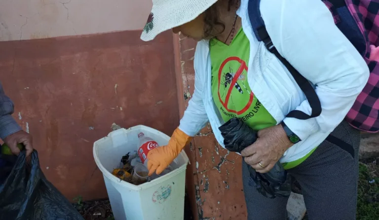 A imagem mostra uma mulher tirando a água parada de recipientes.