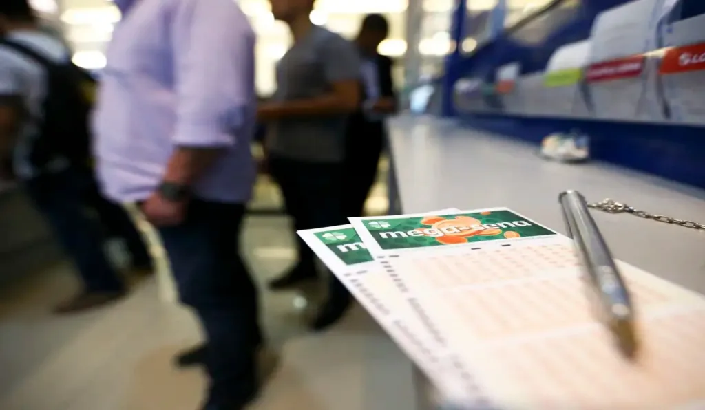 Mega-Sena em cima do balcão em lotérica, com pessoas ao fundo.