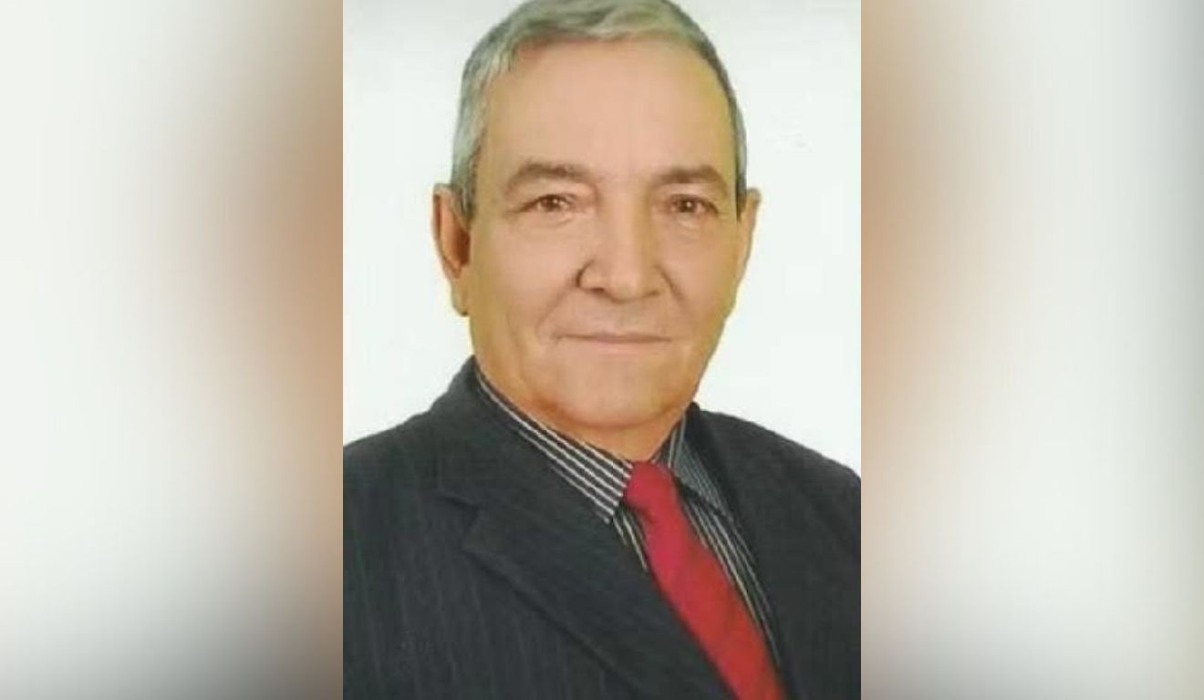 foto de um homem com cabelo branco, terno preto e gravata vermelha