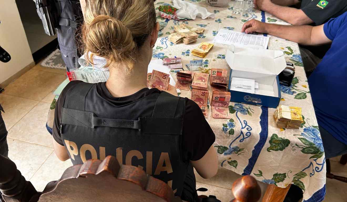 Policiais federais contando notas de dinheiro durante operação que investiga fraudes no programa Farmácia Popular.