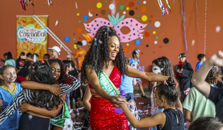 Pessoas comemorando o carnaval. No centro da imagem há uma mulher dançando com uma criança.