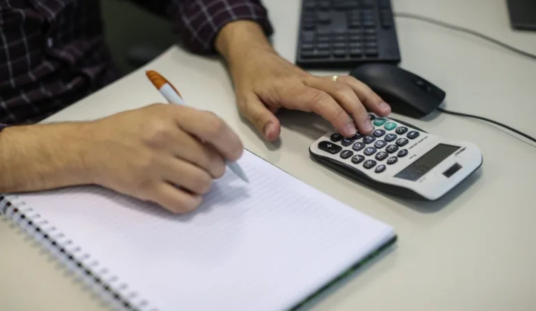pessoa fazendo contas em um caderno com ajuda de calculadora