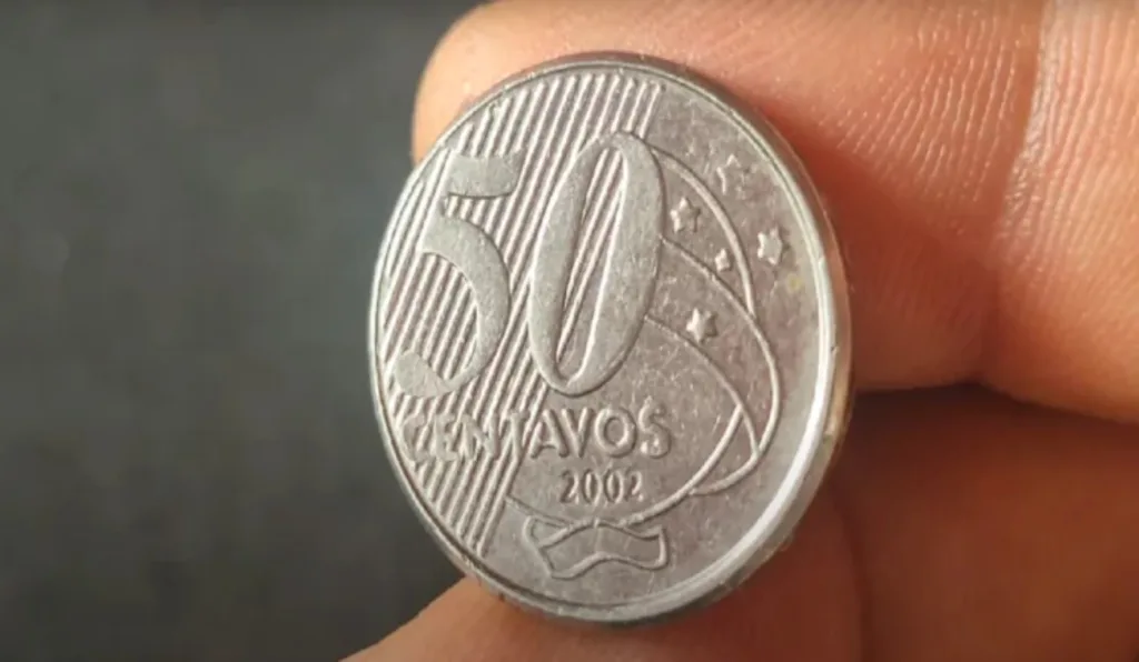 Dedos segurando moeda de 50 centavos de 2002.