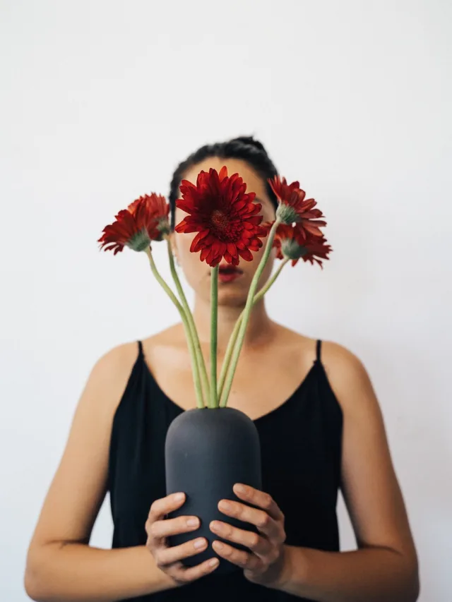 Mulher escondida atrás margaridas vermelhas.