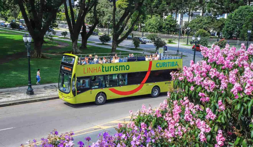 Linha de Turismo com passageiros em rua florida de Curitiba.