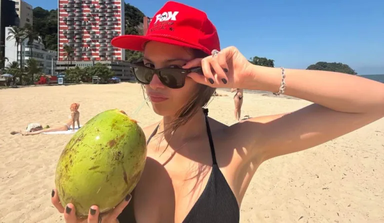Olivia Roldrigo de boné vermelho e óculos preto em areia de Caiobá.