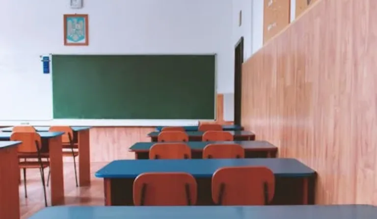Imagem de uma sala de aula com cadeiras, mesas e quadro.