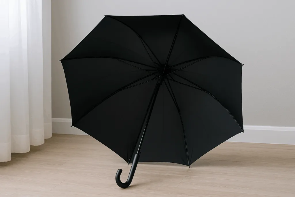 Guarda-chuva preto totalmente aberto secando sobre piso de madeira clara em ambiente ventilado.