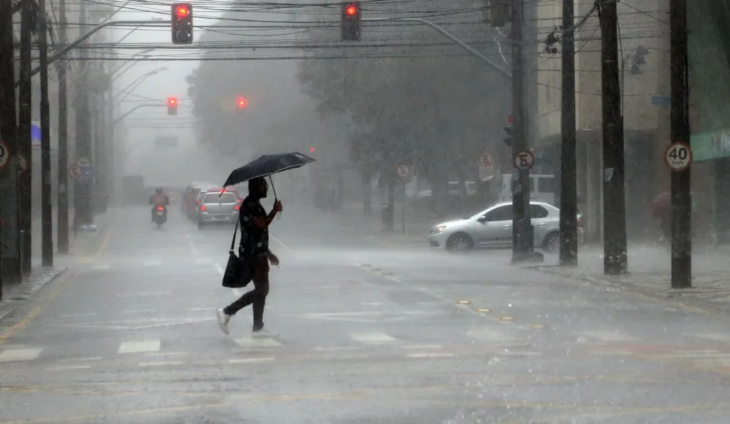 pessoa de sombrinha andando na chuva para ilustrar a chegada do ciclone extratropical