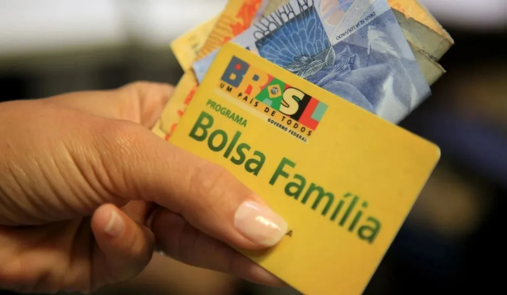 mão segurando cartão do bolsa familia junto com dinheiro