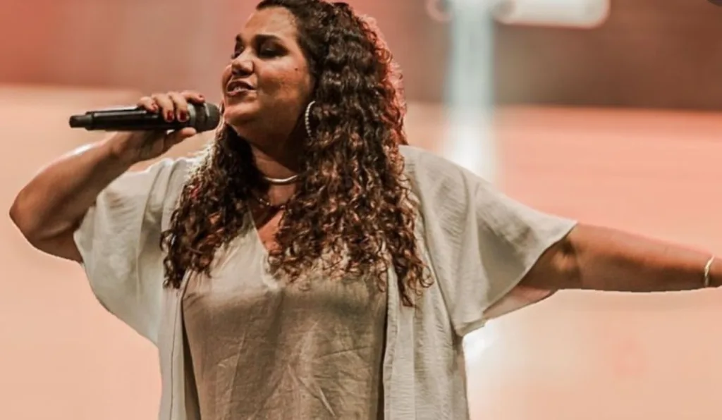 Mulher de cabelo cacheado cantando. Eliana participa no Santo Rosário