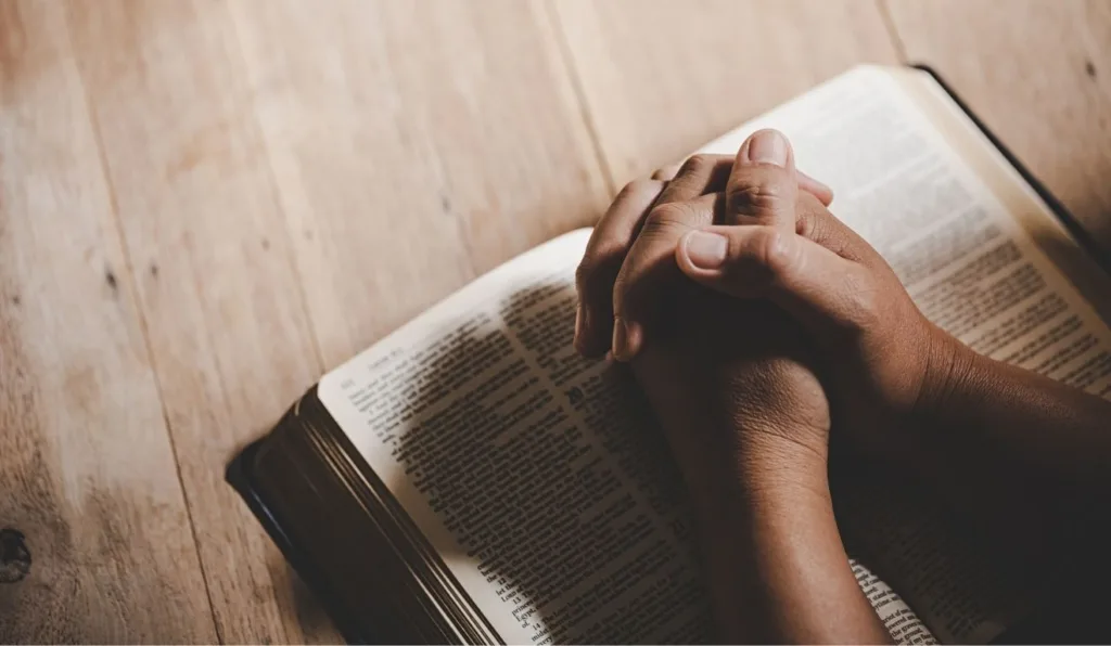 pessoa orando em frente a uma biblia