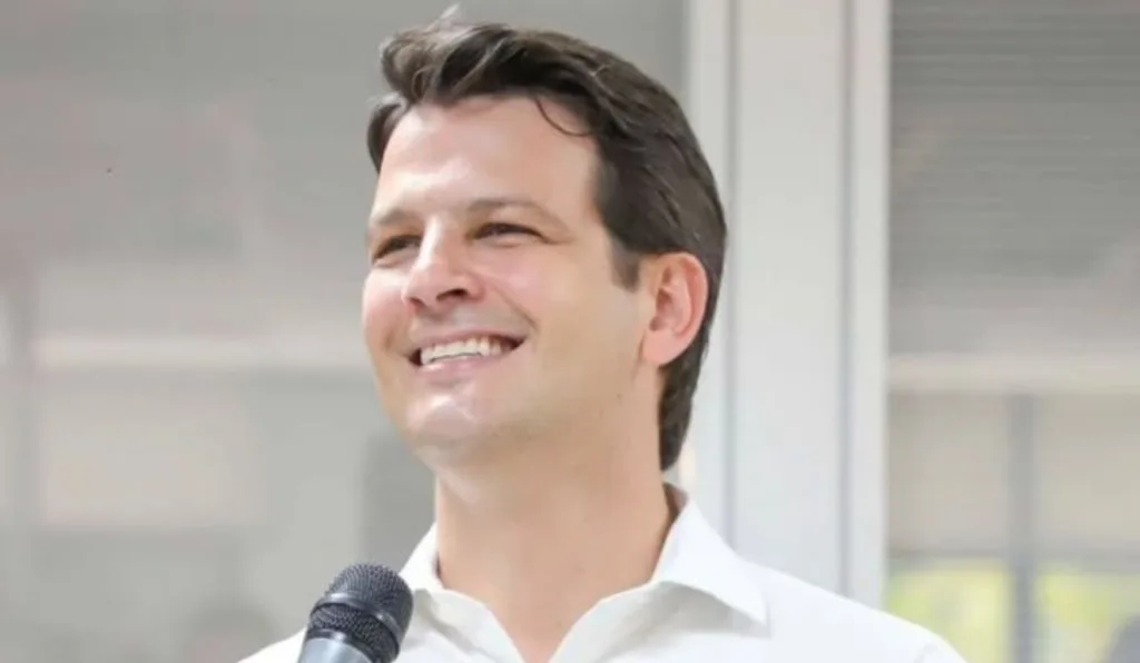 foto de um homem branco de camisa branca segurando um microfone