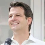 foto de um homem branco de camisa branca segurando um microfone