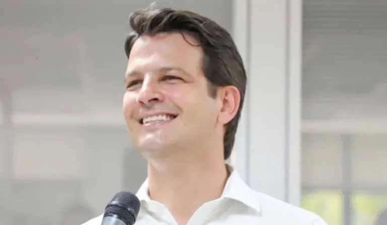 foto de um homem branco de camisa branca segurando um microfone