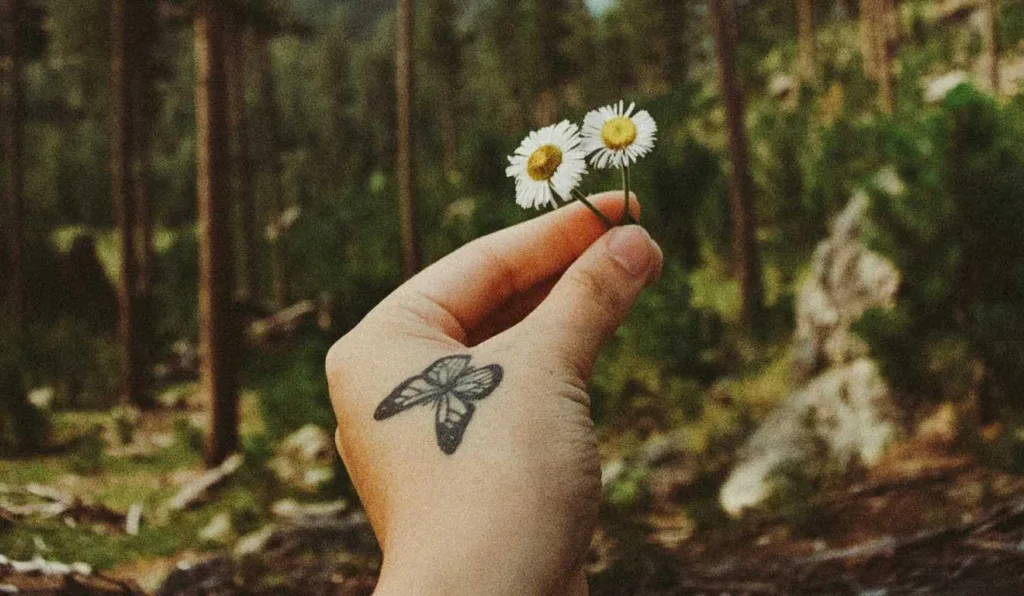 Tatuagem de borboleta na mão que segura uma flor