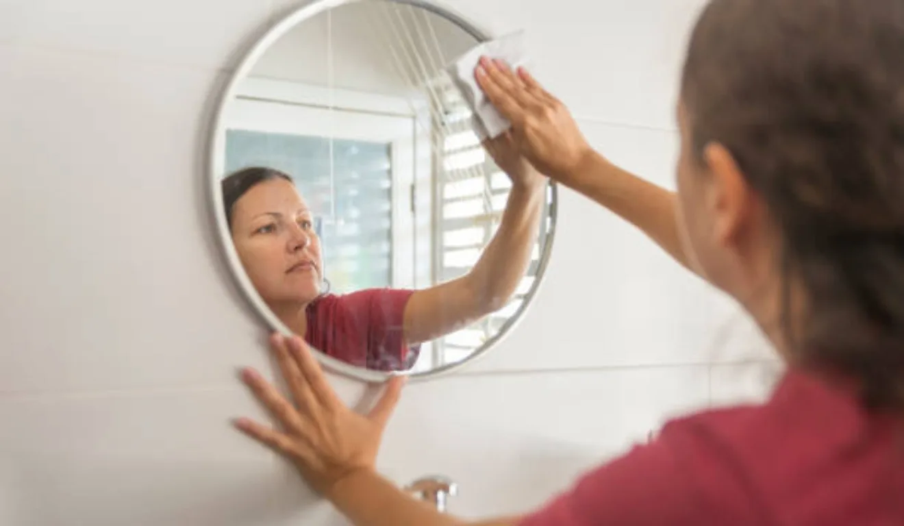 Mulher limpando espelho.
