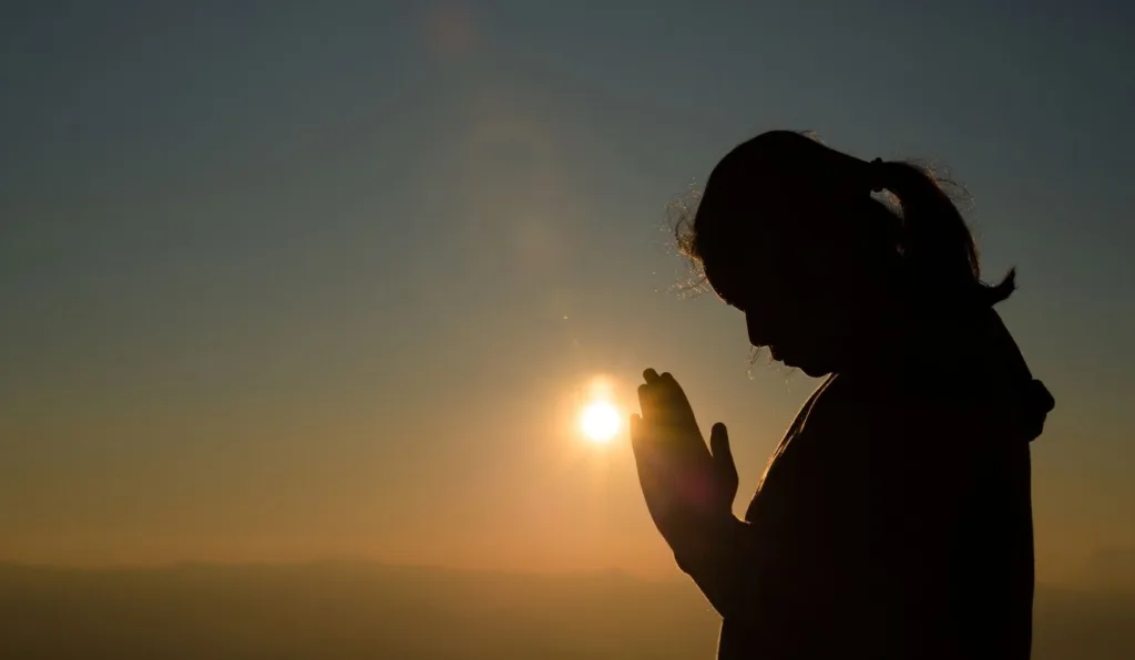 silhueta de mulher orando em frente ao sol