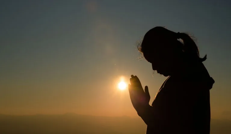 silhueta de mulher orando em frente ao sol