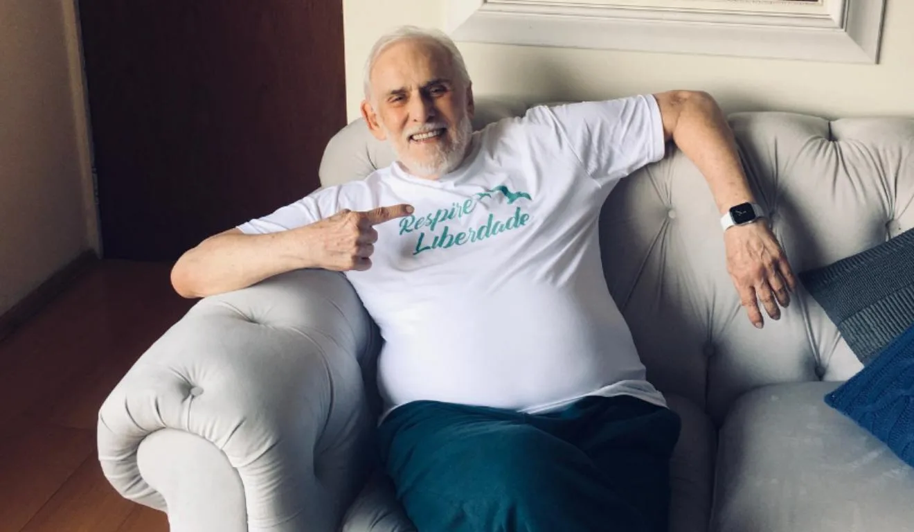 Francisco Cuoco sentado no sofá apontando para a camiseta