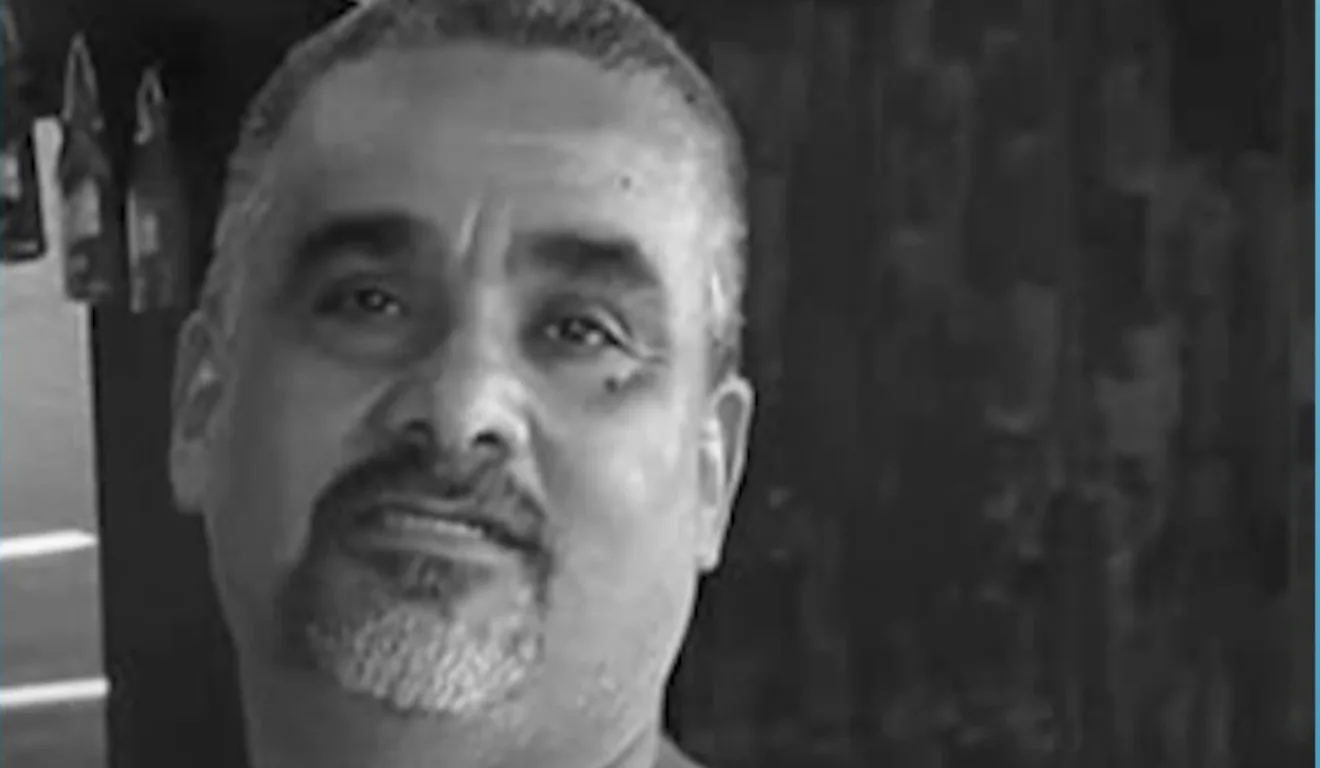 Alfredo Bueno sorri levemente em uma foto em preto e branco, usando camiseta regata.