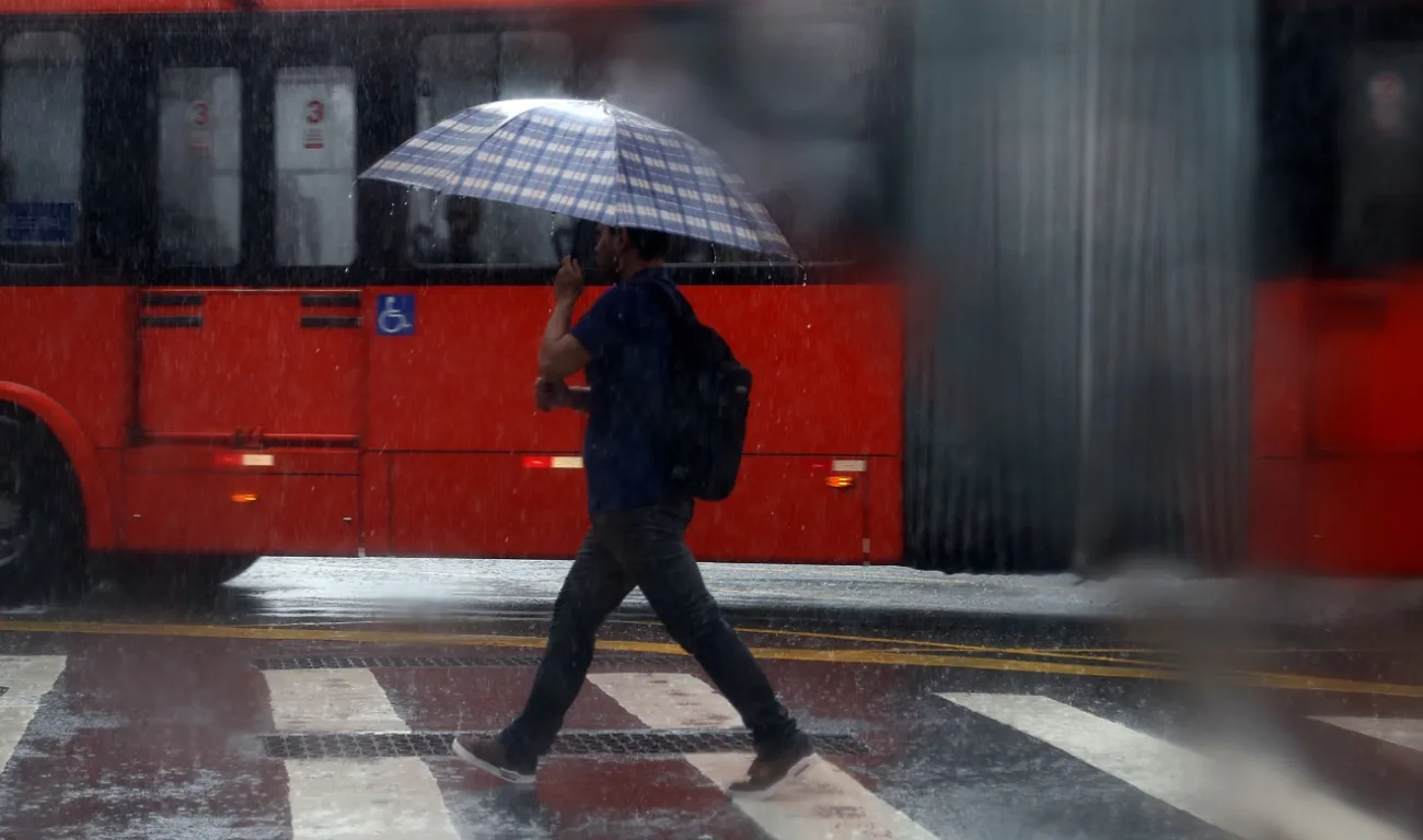 homem de guarda chuva passando em frente ao ônibus