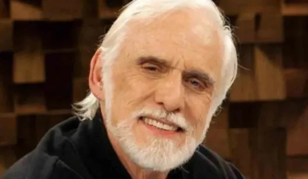 Ator Francisco Cuoco com uma camisa preta e sorrindo para a foto durante a gravação de um programa de televisão