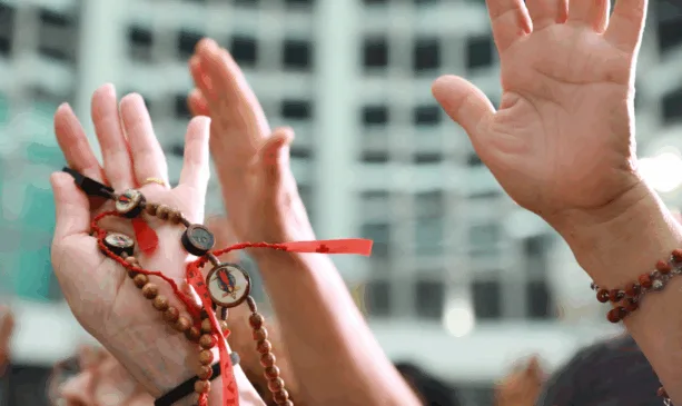 mão de fiéis para cima com terço na mão