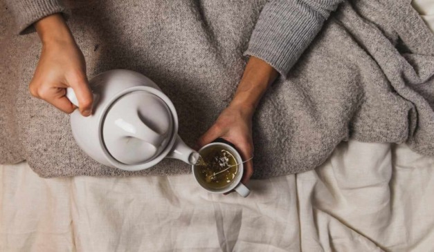 pessoa servindo uma xícara de chá na cama