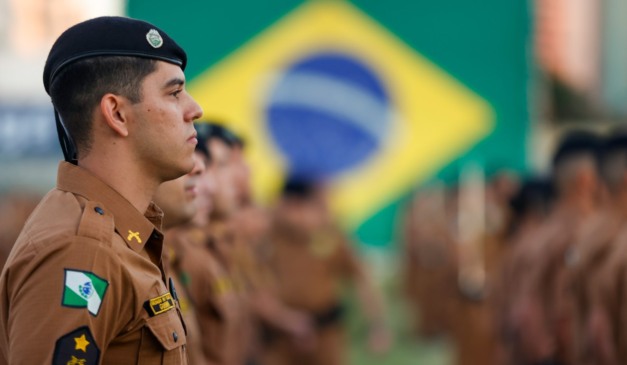 Policiais militares do paraná perfilados com a bandeira do brasil no fundo