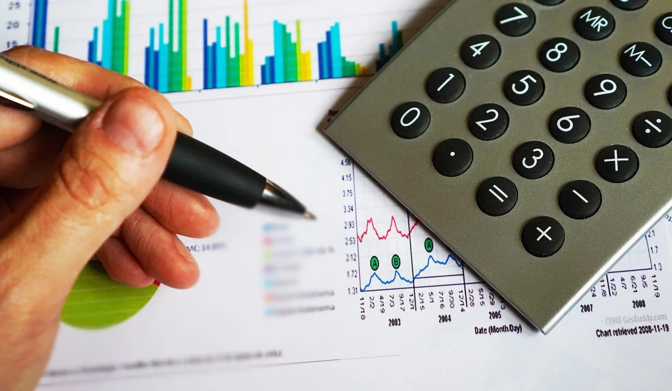 mão com caneta ao lado de gráfico e calculadora