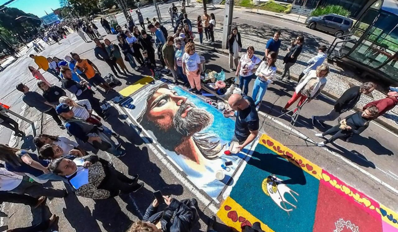 Imagem do tapete colorido tradicional de Corpus Christi, com diversas pessoas por perto.