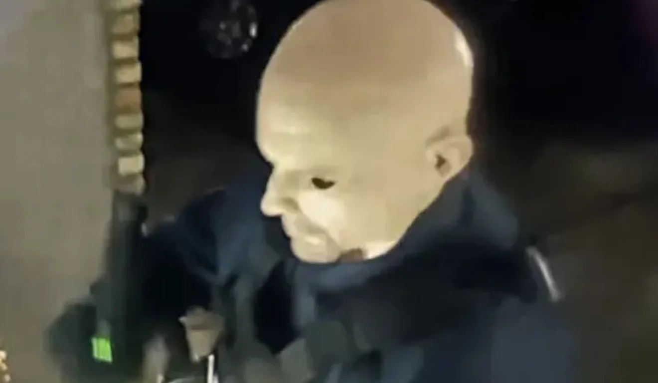 Homem mascarado com arma em punho, vestindo colete tático durante a ação.