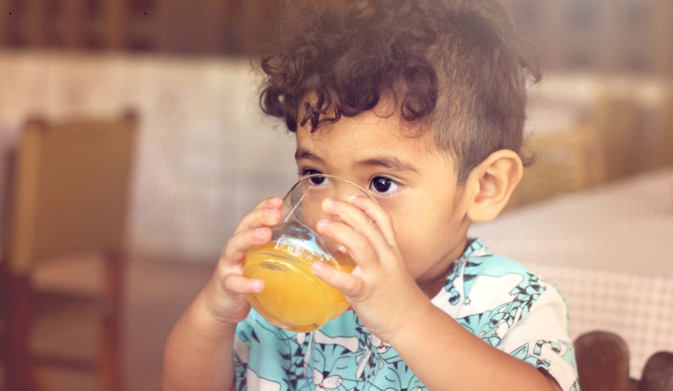 Bebê tomando suco em copo de vidro