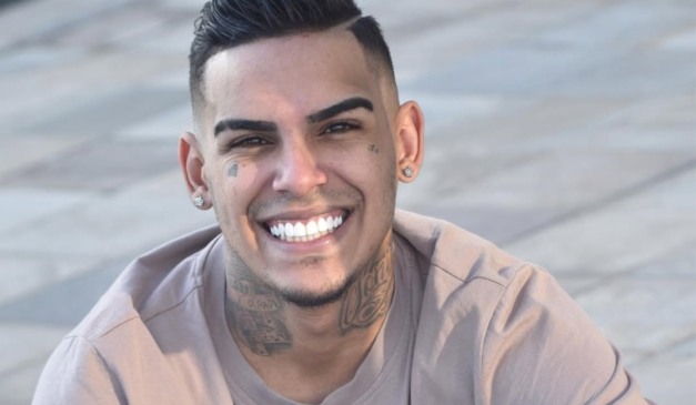 MC Paulinho DK em foto sorrindo, com uma camisa marrom