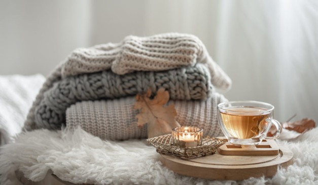 Blusas de lã e xícara em cima da cama.