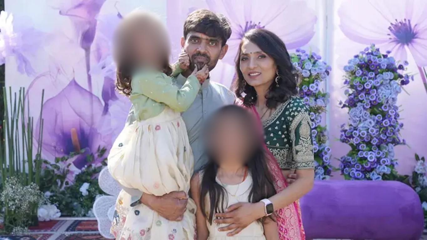 Família indiana posa para foto em evento ao ar livre, com decoração em tons de roxo e flores. O pai segura uma das filhas no colo, ao lado da esposa e da filha mais velha.