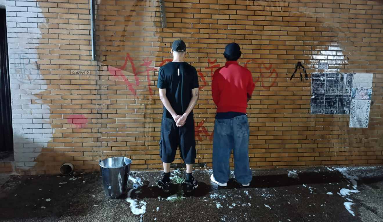 Os dois jovens que picharam o muro de costas, após terminarem de limpar o muro