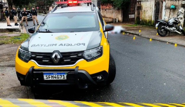 Viatura da Polícia Militar; ao fundo, homem que morreu baleado por 12 tiros em Curitiba.