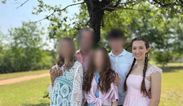 Malaya Hammond sorri usando vestido rosa claro, com os cabelos em tranças, ao lado da família em um ambiente arborizado; os rostos dos outros membros estão desfocados.