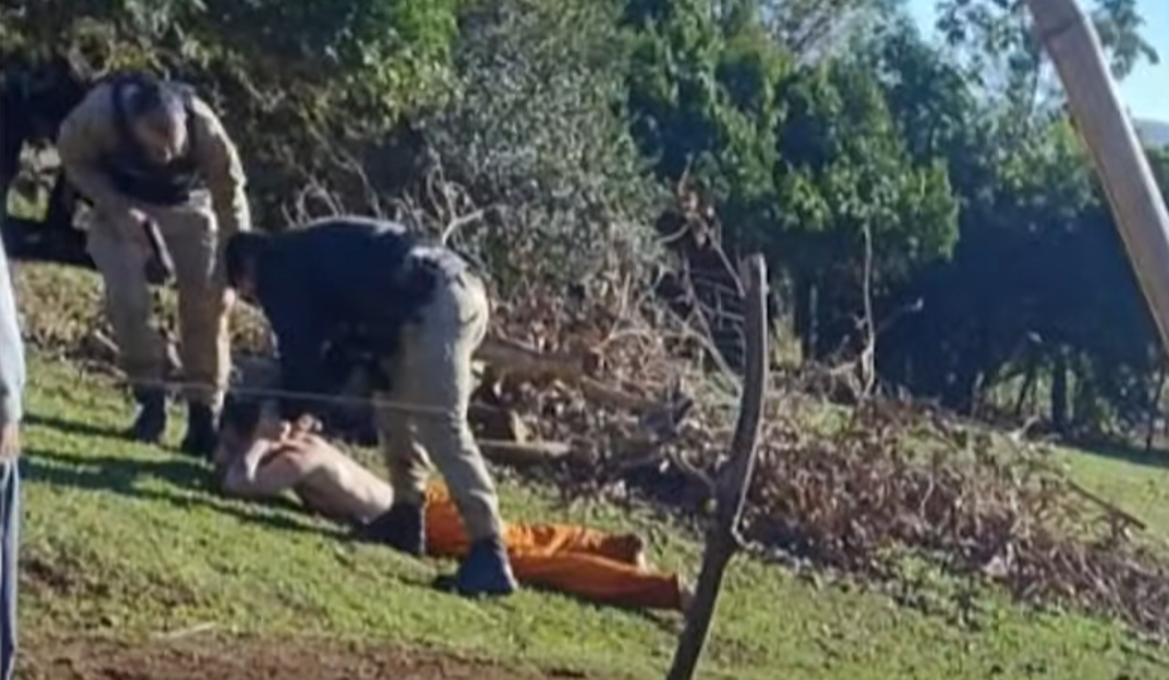 Dois policiais em uma área de mata prendendo um fugitivo.